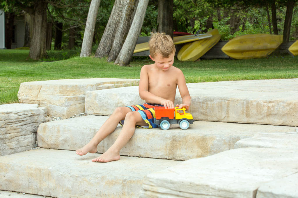 little boy sitting on stone stairs playing with toy truck
