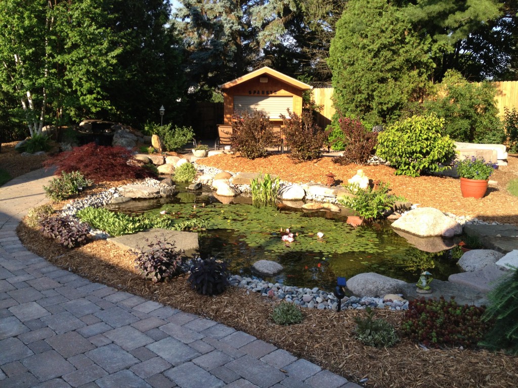 custom pond with large stones encircling the pond, and a custom brick paver driveway.