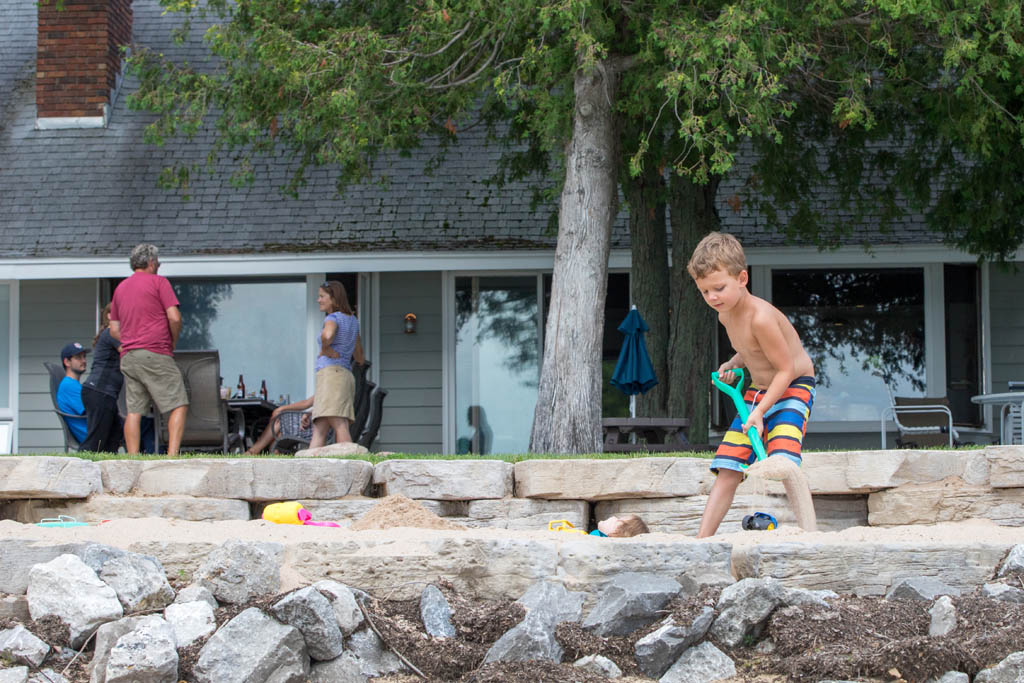 little boy using a green plastic shovel to make a sand castle