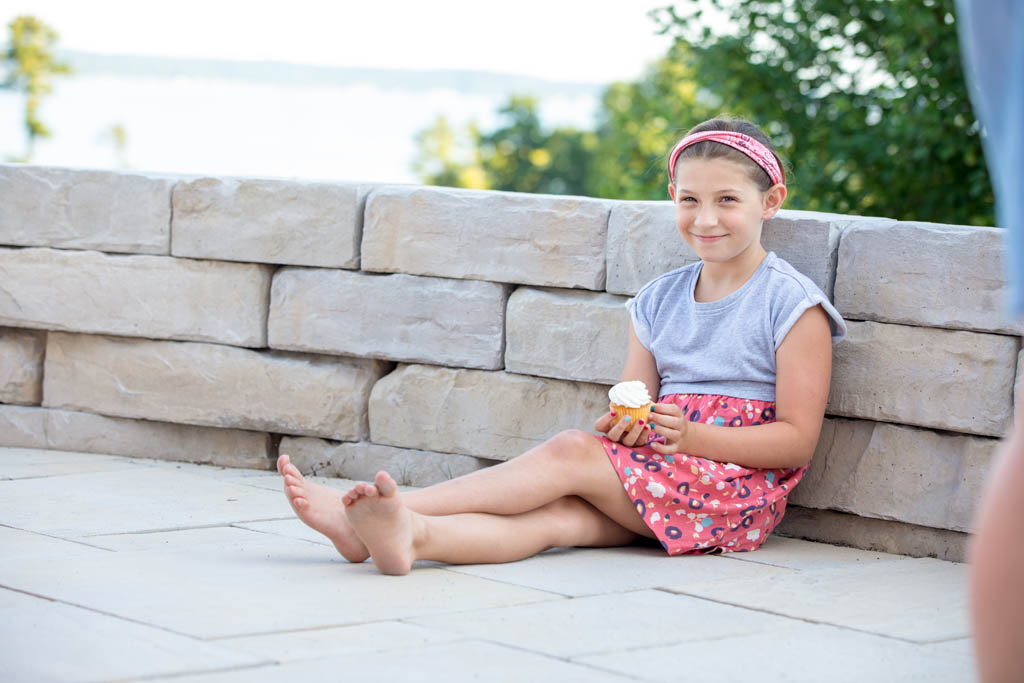 little girl sitting against the wall eating a cupcake